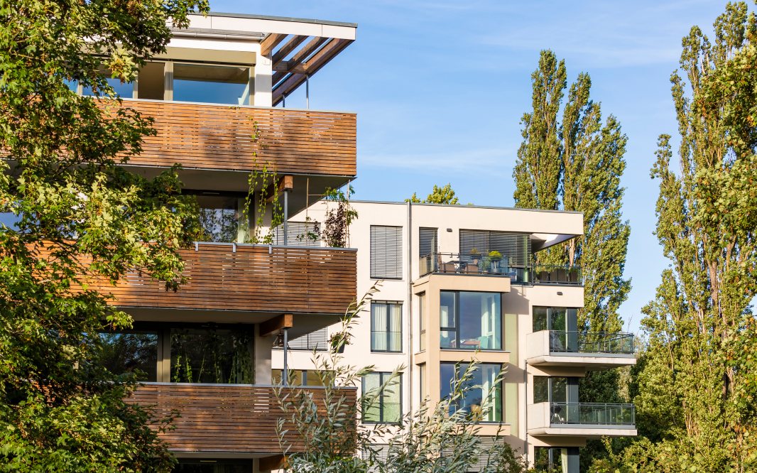 Modern residential buildings with balconies and large windows surrounded by trees under a clear sky