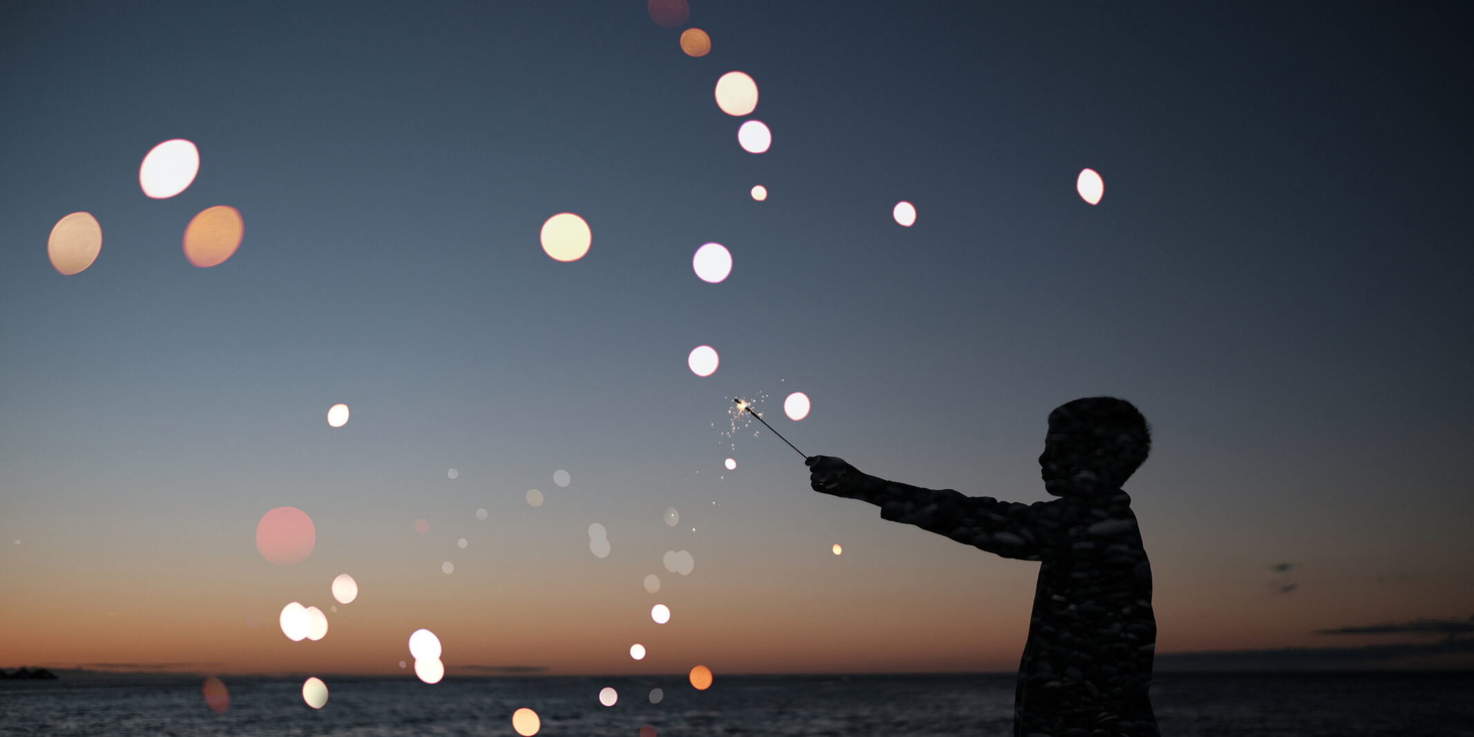 Silhouette of a person standing by the ocean at sunset, reaching toward glowing light spots in the air, with waves and a fading sky in the background